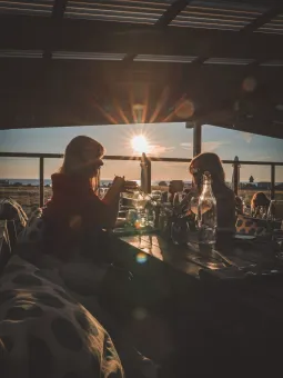 Siluetter av två personer vid ett dukat bord på en terrass, med låg sol och hav i bakgrunden..