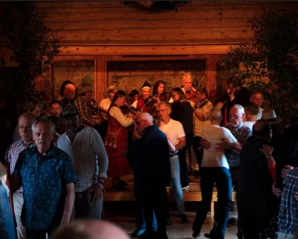 Dansande människor i en lokal, musiker som spelar på en scen, några klädda i folkdräkt.