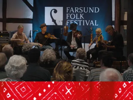 Fem musiker som sitter på en scen och spelar olika instrument, röd detalj från en folkdräkt i bakgrunden