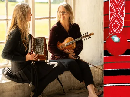 Två kvinnor som sitter i en fönstrsmyg, en av dem håller i en fiol och den andra i ett dragspel, en detalj från en folkdräkt med ränder i rött svart, vitt och grönt samt ett band med en röd tofs.