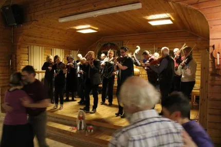 Ett spelmanslag som spelar på en scen, par som dansar framför scenen.