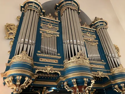 Närbild av stor kyrkorgel med silverfärgade pipor och rikt ornamenterade blå och guldfärgade sniderier..
