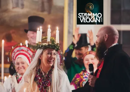 En kvinna med en luciakrona på huvudet, brevid henne en man i svart rock som håller en mikrofon i handen,  två kvinnor i folkräkter, två män i folkdräkt och höga hattar i bakgrunden, logga Stämmoveckan.