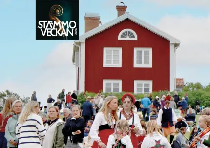 En grupp besökare samlade i en sluttning, några iklädda folkdräkt, någon med ett instrument, i bakgrunden ett rött tvåvåningshus, logga Stämmoveckan,