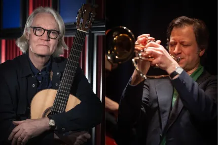 En man i axellångt hår och glasögon iklädd svart skjorta, som håller om en gitarr, en man i mörkt hår iklädd blå kavaj, spelar på en trumpet.