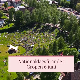 En bild tagen med drönare eller från flygplan, bilden visar en stor grupp människor samlade på en gräsyta, en scen med ett vitt uppspänt segel, en rosa ruta med texten Nationaldagsfirande i Gropen 6 juni.
