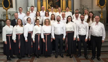 Grupp människor i vita skjortor och mörka kjolar/byxor står uppställda i en kyrka framför altaret..