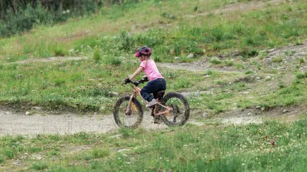 Ett barn med hjälm cyklar på en mountainbike längs en grusig stig i ett grönt, kuperat landskap..