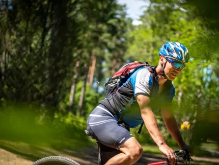 En manlig cyklist iklädd cykelkläder, ryggsäck på ryggen, skog i bakgrunden.