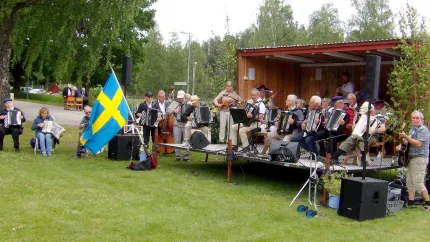 Spelmän på en utomhusscen, en svensk flagga brevid scenen.