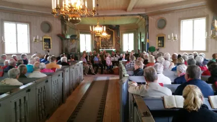 Interiören i en kyrka, fullsatta bänkar, spelmän längst fram i kyrkan.
