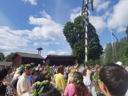 Människor samlade kring en midsommarstång.