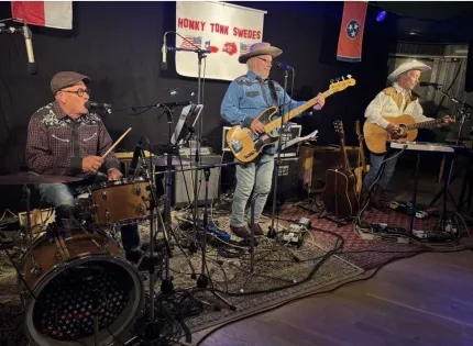 Tre män på en scen, två av dem har cowboyhatt och båda spelar gitarr, den tredje mannen har keps och spelar trummor.