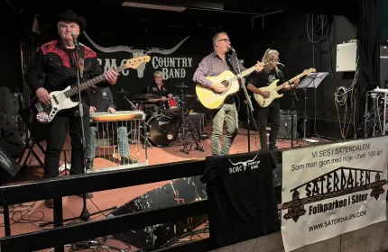 Fem män på en scen, tre spelar gitarr, en spelar trummoroch en spelar keyboard, banderoll DMC Country band.