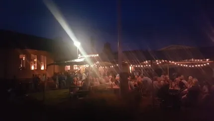 En bild tagen på kvällen, besökare som sitter på en uteservering under tak, ljusslingor.