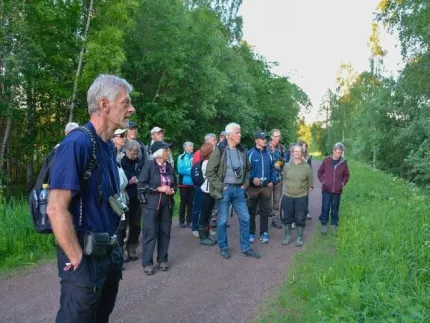 En grupp människor som står på en grusväg, några med kikare.