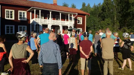 En grupp människor samlade framför en röd träbyggnad i två våningar.