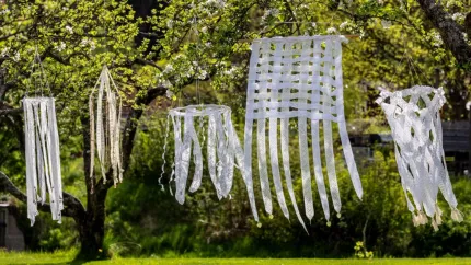 Vita vindspel av spetsband hänger i ett blommande träd i en grön trädgård i solljus..