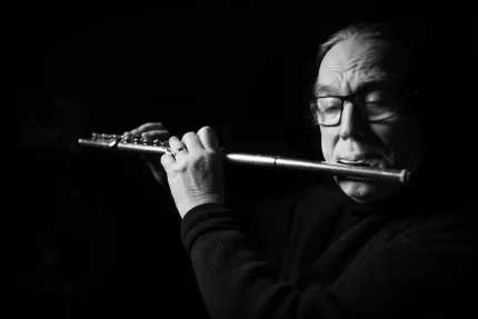 Svartvit bild av en person som spelar tvärflöjt mot mörk bakgrund; händer och instrument är i fokus..