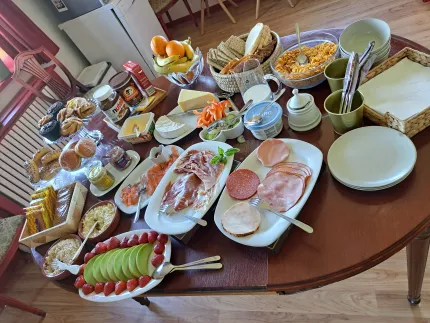 Ett runt bord dukat med bröd, pålägg, ost, frukt, yoghurt, müsli och porslin i ett kök..