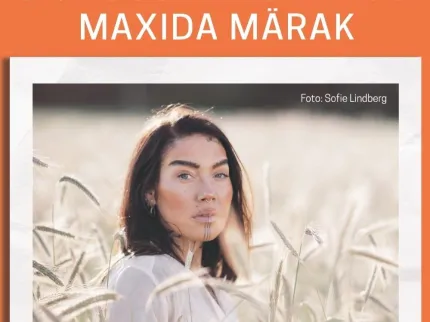 En kvinna med långt mörkt hår står i ett solbelyst gräsfält och ser mot kameran, med mjuk bakgrund..