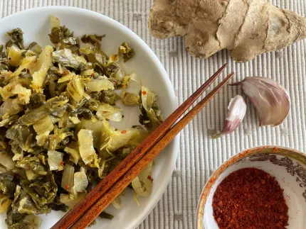 Vit tallrik med hackad picklad grönsak och ätpinnar, bredvid ingefära, vitlöksklyftor och chiliflakes..