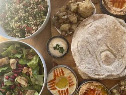 Toppvy av ett mezebord med pitabröd, hummus, sallader, rostad blomkål och små skålar med dippar..
