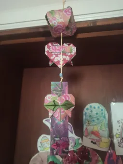 Hängande origamiprydnad med blommigt papper i flera delar på ett snöre, fotograferad inomhus mot dörr och teckningar..