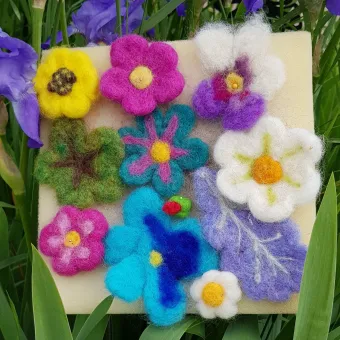 Färgglada tovade blommor och en fjäril fästa på en ljus filtbit, placerad bland gröna blad och lila blommor..