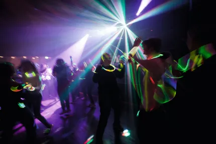 Mörk klubbscen med dansande människor, färgade laserstrålar och lysarmband som skapar starka ljusspår..