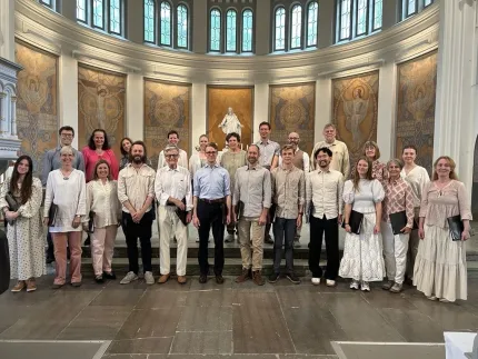 Grupp människor står uppställda i en kyrka framför altare med staty, mosaikväggar och höga fönster.