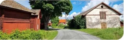 En smal asfaltsväg i bymiljö, med röda träbyggnader till vänster och en ljus lada till höger.