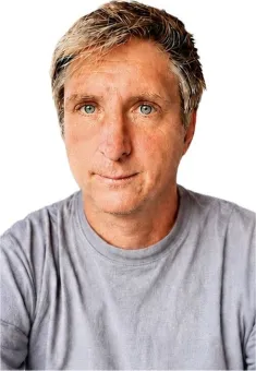 Närbildsporträtt av en medelålders man med grått hår och grå t-shirt mot vit bakgrund..