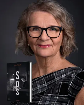 Studioportätt av en äldre kvinna med glasögon och grått hår som håller upp en bok mot mörk bakgrund..