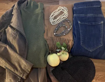 Platt upplägg med grå jacka, grön polotröja, beige halsduk med pärlhalsband, blå jeans, mössa och äpplen..