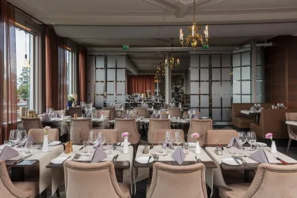Ljusa matsalen i en restaurang med dukade bord, vinglas, servetter och ljuskronor, stora fönster till vänster..