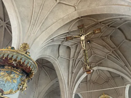 Interiör i en kyrka med kryssvälvt tak och ett hängande krucifix, samt en rikt dekorerad predikstol till vänster..