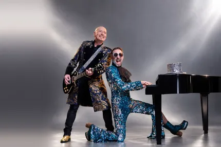 Två musiker i glittriga scenkläder, en spelar elgitarr och en spelar flygel i studiomiljö..