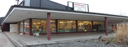 Byggnad med en rad med fönster, skylt Hildings second hand på taket,  högre svart byggnad i bakrunden.