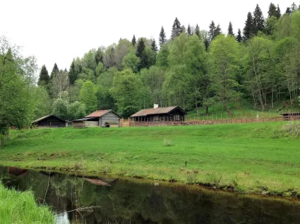 Ljusterån flyter förbi fäboden med timrade stugor.
