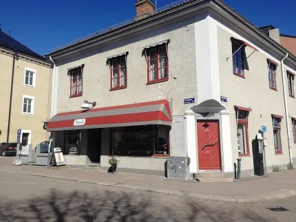 Exteriörbild på caféet med vit murad fasad och randiga markiser ovanför fönstren.