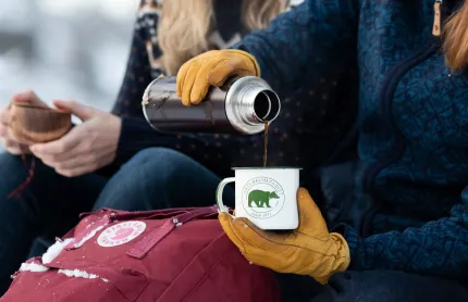 Några som äter matsäck utomhus, med ryggsäck, termos och kåsa.