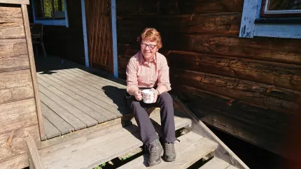 Dam i vandringskläder och kängor sitter på ett traffsteg och dricker kaffe.