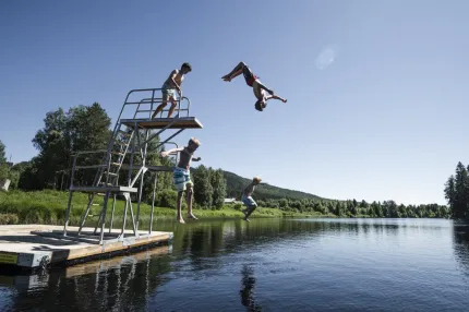 Four boys jump into the water from the trampoline.