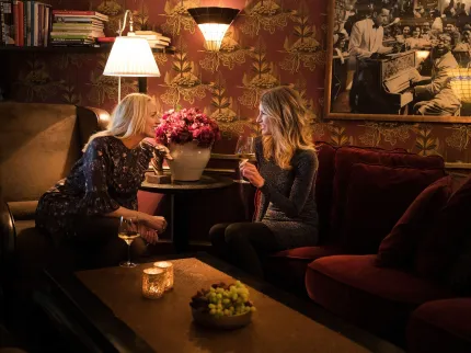 Två damer sitter och pratar mittemot varandra med tända lampor i ett mörkt rum. 