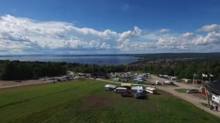 En grupp husbilar parkerade på ett fält nära ett vattendrag.