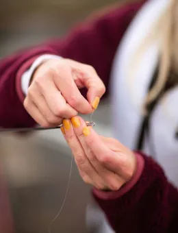 Hands tying a fly on fishing rod.