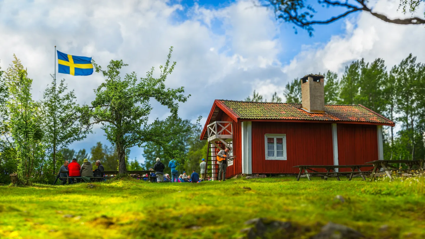 Rödmålad stuga med en flaggstång på gården.