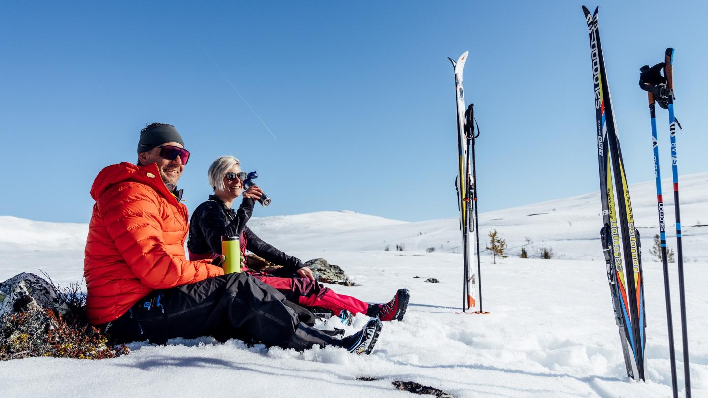 Par som njuter i snön av solen vid sina skidor.
