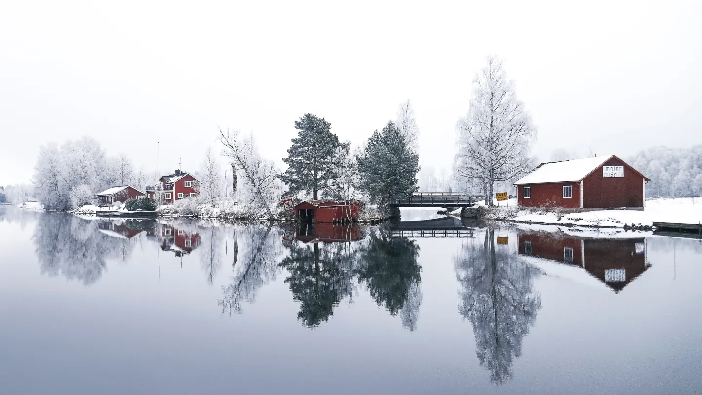 Vintrig vy över stugor och träd som speglas i vatten.